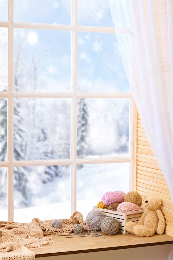 Woolen yarn and fabric on the window sill. Beautiful view outside the window - winter landscape and snow.