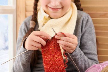 Kız çocuk yün iplikler ile bir pencere pervazına oturan ve örgü. Güzel manzara pencere dışında-güneşli bir günde kış ve kar.