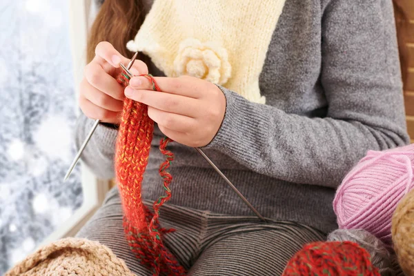 Kız çocuk yün iplikler ile bir pencere pervazına oturan ve örgü. Güzel manzara pencere dışında-güneşli bir günde kış ve kar.
