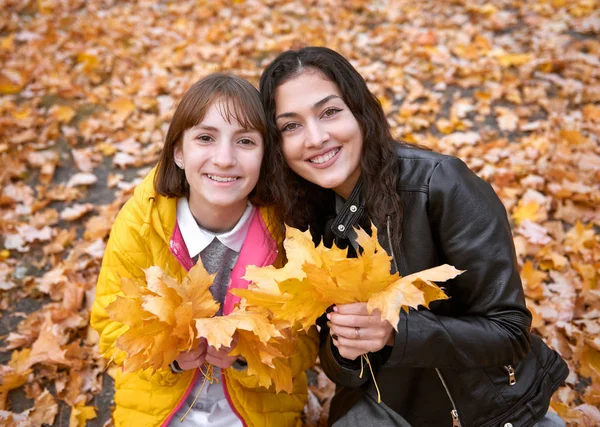 きれいな女性および十代女の子秋の公園でカエデの葉の束でポーズをとっています 秋のシーズンで美しい風景 — ストック写真