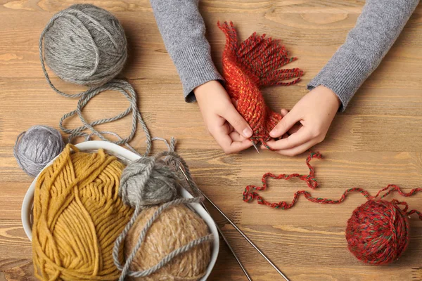 Child girl is learning to knit. Colorful wool yarns are on the wooden table. Hand closeup.