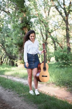 ormanda yürüyüş ve iskambil gitar, yaz doğa, parlak güneş ışığı, gölgeler ve yeşil yaprakları, romantik duygular genç kadın