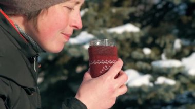Kadın ormanda, güzel kış manzara karlı köknar ağaçları ile sıcak çay içiyor.
