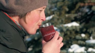 Kadın ormanda, güzel kış manzara karlı köknar ağaçları ile sıcak çay içiyor.