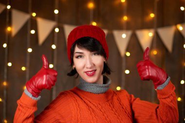 Güzel kadın koyu ahşap arka plan, Noel ışıkları ve bayraklar, tatil kavramı üzerinde poz. Kırmızı örgü şapka ve kazak giymiş.