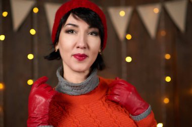 Güzel kadın koyu ahşap arka plan, Noel ışıkları ve bayraklar, tatil kavramı üzerinde poz. Kırmızı örgü şapka ve kazak giymiş.