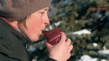 Kadın ormanda, güzel kış manzara karlı köknar ağaçları ile sıcak çay içiyor.