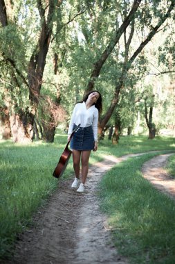 ormanda yürüyüş ve iskambil gitar, yaz doğa, parlak güneş ışığı, gölgeler ve yeşil yaprakları, romantik duygular genç kadın
