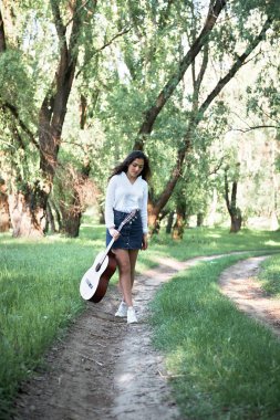 ormanda yürüyüş ve iskambil gitar, yaz doğa, parlak güneş ışığı, gölgeler ve yeşil yaprakları, romantik duygular genç kadın