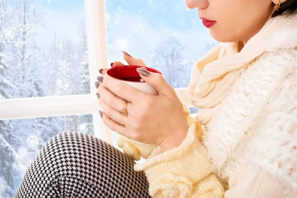 女人坐在窗台上拿着茶杯 窗外美丽的景色 冬日森林和雪中阳光明媚的一天 — 图库照片
