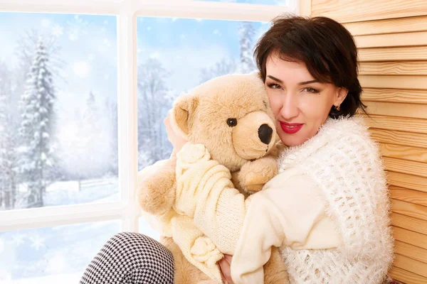 女人坐在窗台上 带着熊玩具 窗外美丽的景色 冬日森林和雪中阳光明媚的一天 — 图库照片