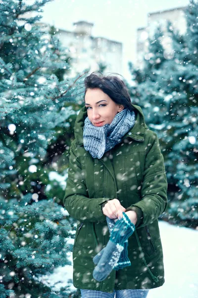 woman is wearing mittens in winter forest, green fir trees with snow