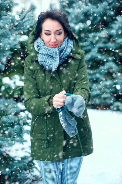 woman is wearing mittens in winter forest, green fir trees with snow