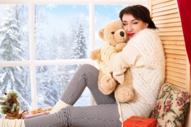 Kadın ayı oyuncak bir pencere pervazına üzerinde oturuyor. Güzel manzara pencere dışında-güneşli bir günde kış orman ve kar.