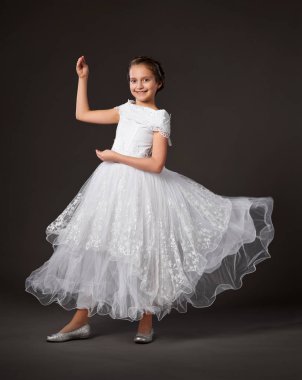 küçük kız bir beyaz topu cüppe, koyu arka plan dans ediyor