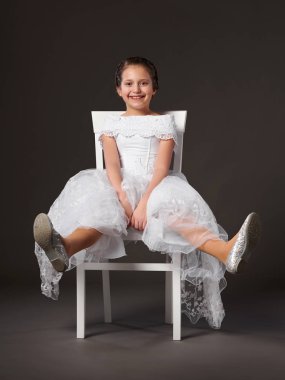 bir beyaz topu elbisesi giymiş ve iskemlede koyu arka plan küçük kız