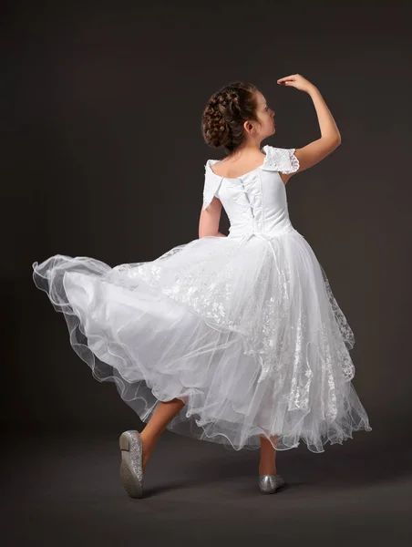 Lille jente danser i hvit ballkjole, mørk bakgrunn – stockfoto