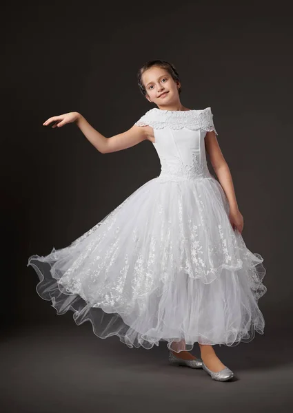 Liten flicka dansar i en vit balklänning, mörk bakgrund — Stockfoto
