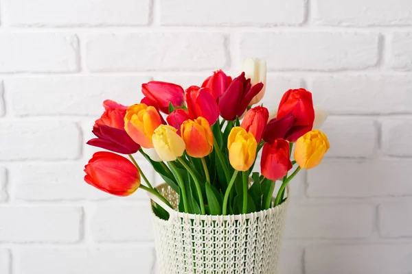 Tulipán flores están en una cesta sobre la mesa, pared de ladrillo blanco como fondo — Foto de Stock