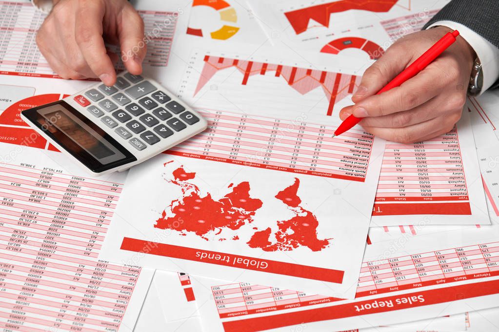 Businessman accountant using calculator for calculating finance on desk office. Business financial accounting concept Red reports and graphs. Office employee examines schedules and reports.