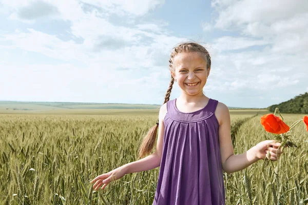 Fată cu flori de lalele roșii care pozează în câmpul de grâu, soare strălucitor, peisaj frumos de vară — Fotografie, imagine de stoc