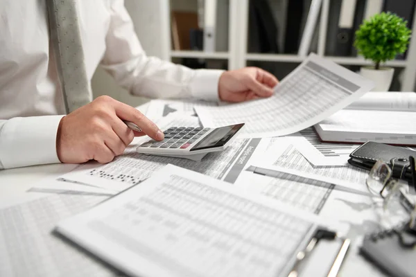 Omul de afaceri care lucrează la birou și calculează finanțele, citește și scrie rapoarte. Conceptul de contabilitate financiară . — Fotografie, imagine de stoc
