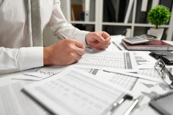 Omul de afaceri care lucrează la birou și calculează finanțele, citește și scrie rapoarte. Conceptul de contabilitate financiară . — Fotografie, imagine de stoc
