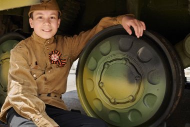 İkinci Dünya Savaşı sırasında Sovyet askeri üniforması giymiş çocuk ordu tankı yakınında poz