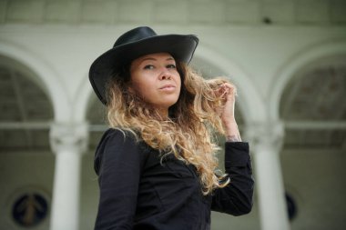 siyah gömlek, şapka ve geniş pantolon eski beyaz evin yakınında poz giymiş şık kız