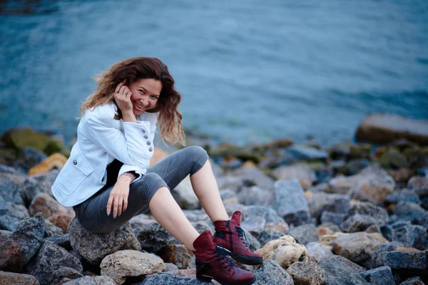 Chica de moda vestida con chaqueta blanca y pantalones anchos posando cerca del mar por la noche —  Fotos de Stock