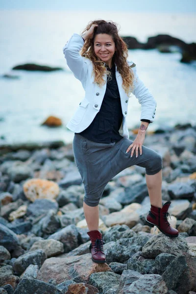 Chica de moda vestida con chaqueta blanca y pantalones anchos posando cerca del mar por la noche —  Fotos de Stock