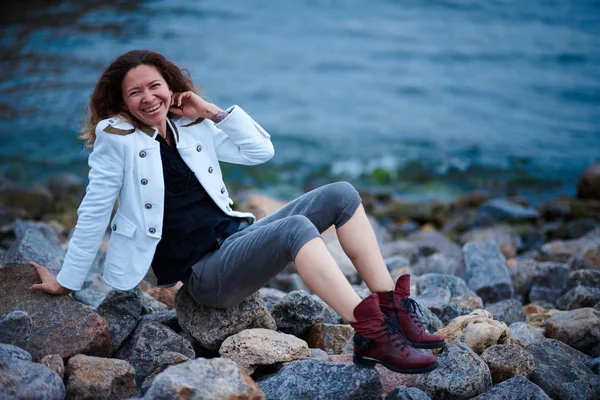 Chica de moda vestida con chaqueta blanca y pantalones anchos posando cerca del mar por la noche —  Fotos de Stock