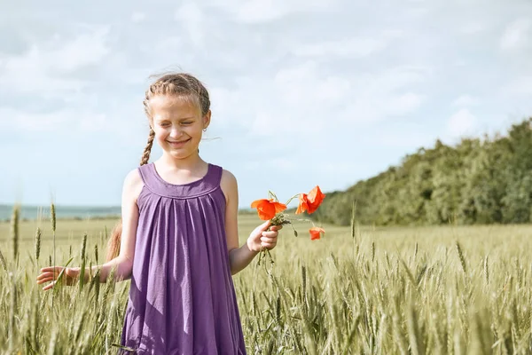 Fată cu flori de lalele roșii care pozează în câmpul de grâu, soare strălucitor, peisaj frumos de vară — Fotografie, imagine de stoc