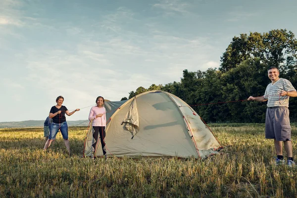 Family set up tent camp at sunset, beautiful summer landscape. Tourism, hiking and traveling in nature.