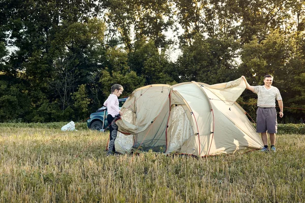 Family set up tent camp at sunset, beautiful summer landscape. Tourism, hiking and traveling in nature.