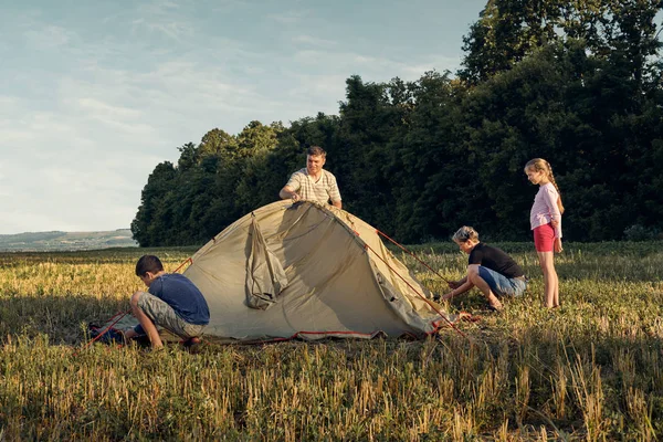 Family set up tent camp at sunset, beautiful summer landscape. Tourism, hiking and traveling in nature.