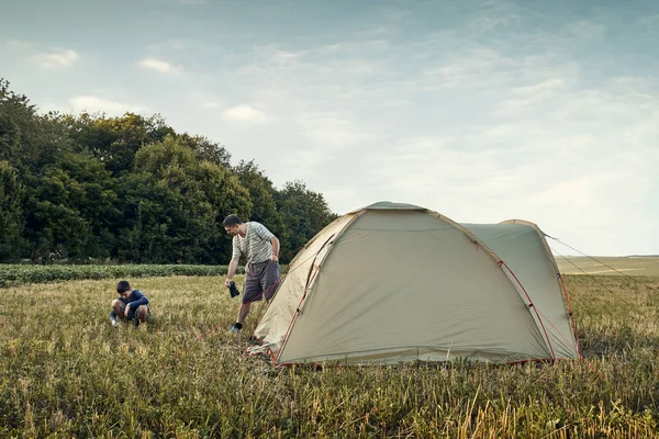 Family set up tent camp at sunset, beautiful summer landscape. Tourism, hiking and traveling in nature.