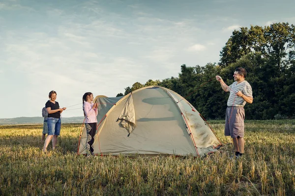 Family set up tent camp at sunset, beautiful summer landscape. Tourism, hiking and traveling in nature.