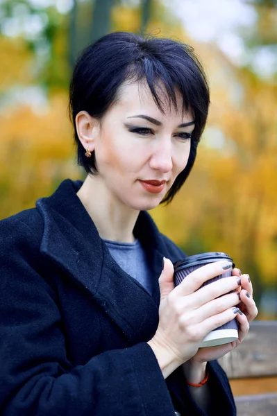 Mulher bonita posando e sonhando com xícara de café no outono parque da cidade, temporada de outono, folhas amarelas — Fotografia de Stock