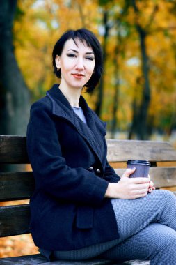 Sonbahar şehir parkında kahve ile oturan güzel kadın, sonbahar sezonu, sarı yapraklar