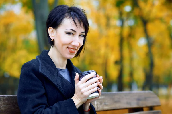 Mulher bonita sentada com café no parque da cidade de outono, estação de outono, folhas amarelas — Fotografia de Stock