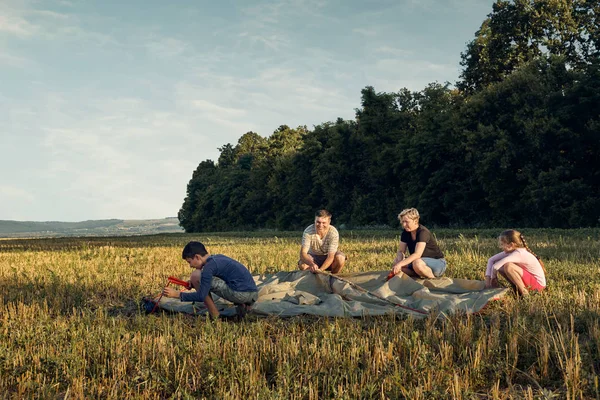 Family set up tent camp at sunset, beautiful summer landscape. Tourism, hiking and traveling in nature.