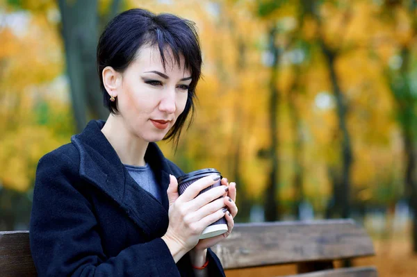 Mulher bonita posando e sonhando com xícara de café no outono parque da cidade, temporada de outono, folhas amarelas — Fotografia de Stock
