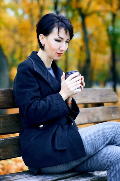 Mulher bonita sentada com café e sonhando no parque da cidade de outono, estação de outono, folhas amarelas — Fotografia de Stock