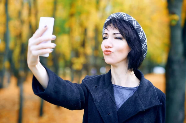 Beautiful woman taking selfie by smartphone and having fun in autumn city park, fall season, yellow leaves — Stock Photo, Image