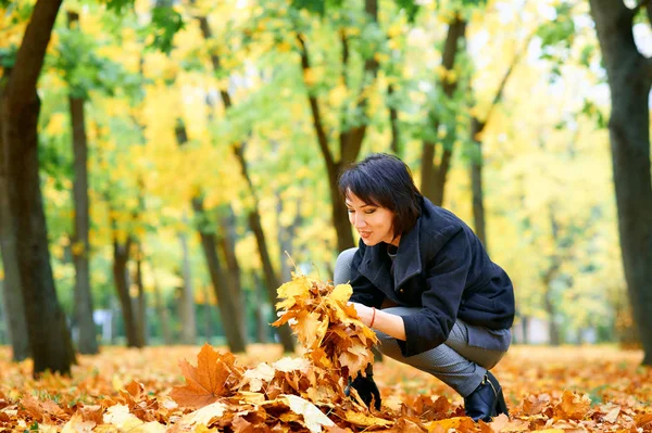 Beautiful woman posing with yellow leaves in autumn city park, fall season — Stock Photo, Image