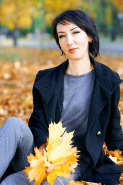 Sonbahar şehir parkında sarı yapraklarla poz veren güzel kadın, sonbahar mevsimi