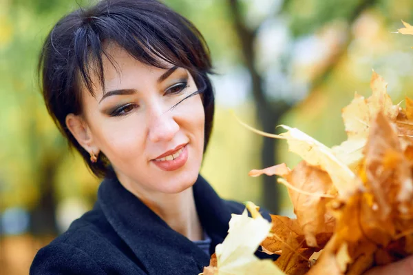 Beautiful woman posing with yellow leaves in autumn city park, fall season — Stock Photo, Image