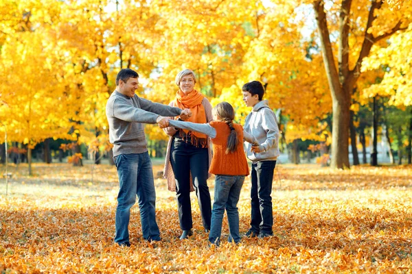 Mutlu aile poz, oyun ve sonbahar şehir parkında eğlenmek. Çocuklar ve ebeveynler birlikte güzel bir gün geçiriyorlar. Ağaçlarda parlak güneş ışığı ve sarı yapraklar, sonbahar mevsimi. — Stok fotoğraf