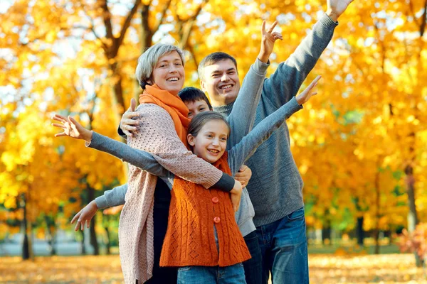 Famiglia felice posa, giocare e divertirsi nel parco della città di autunno. Bambini e genitori insieme hanno una bella giornata. Luce solare brillante e foglie gialle sugli alberi, stagione autunnale . — Foto Stock